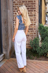 Woman in denim top and white pants standing against a brick wall.